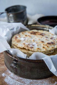 two flat breads in a metal pan on top of a wooden table covered with wax paper