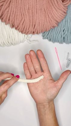 two hands holding yarn and crochet hooks on top of a white surface