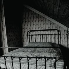 an old iron bed in the corner of a room with floral wallpaper on the walls