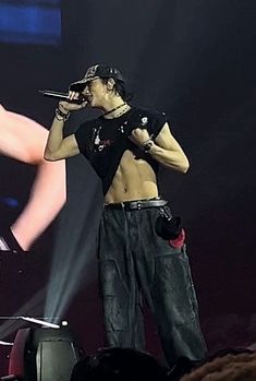 a man standing on top of a stage holding a microphone to his ear and wearing black pants