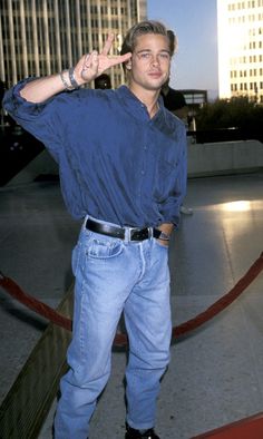 a man in blue shirt and jeans standing next to a red carpet with buildings behind him