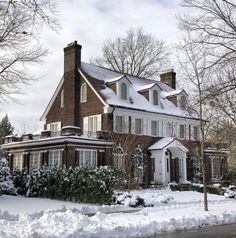 a large brick house covered in snow next to trees and bushes with no leaves on it