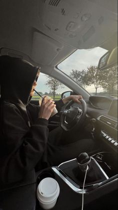 a woman driving a car while holding a cell phone to her ear and wearing a hoodie