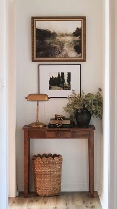 a wooden table sitting under a painting next to a basket on top of a hard wood floor