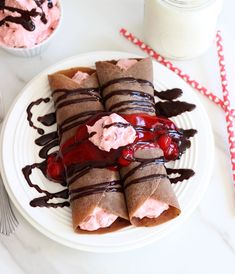 a white plate topped with chocolate crepes covered in strawberry ice cream and drizzle