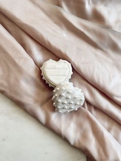 a heart shaped brooch sitting on top of a pink satin fabric covered bed sheet