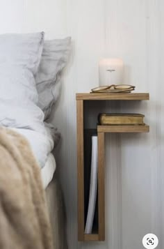 a bedside table with a candle on it next to a white wall and a bed