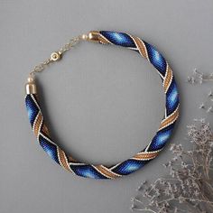 a blue and white bracelet with gold accents on a gray surface next to dried flowers