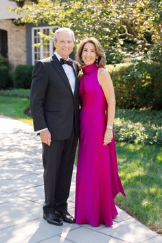 an older man and woman in formal wear posing for a photo outside their home on a sunny day