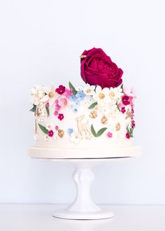 a white cake decorated with flowers and a single red rose sitting on top of it