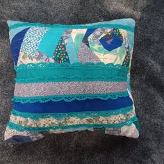 a blue and white patchwork pillow sitting on top of a gray carpeted floor