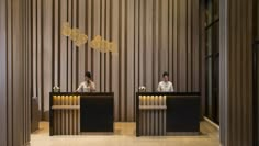 two people sitting at the front desk of a hotel lobby with wooden walls and columns