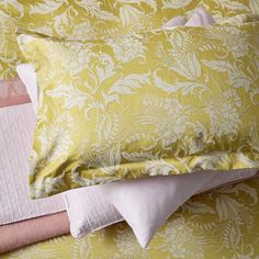 a yellow and pink bed spread with two pillows on top of each other, along with matching sheets