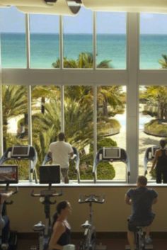 people riding stationary exercise bikes in front of a large window overlooking the beach and ocean