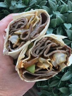 a hand holding a sandwich filled with meat and veggies on top of green leaves