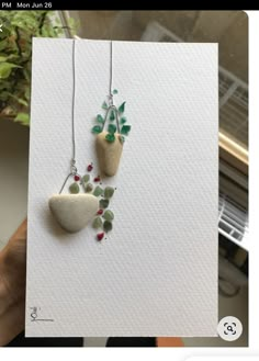 someone holding up a card with two small rocks and flowers hanging from it's sides