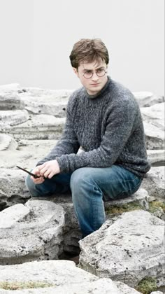 a young man sitting on top of rocks holding a cell phone