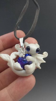 a hand holding a white and blue necklace with an angel figurine on it