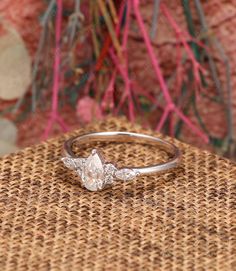 a diamond ring sitting on top of a wicker table next to a pink flower