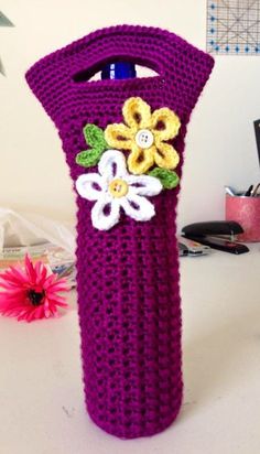 a purple crocheted bag with flowers on it sitting on a table next to a pink flower