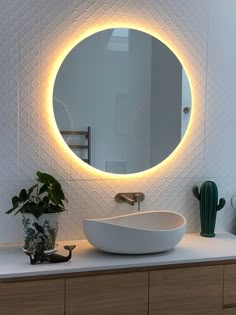 a bathroom sink with a round mirror above it and plants on the counter top next to it