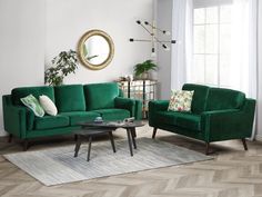 a living room with two green couches and a coffee table in front of a round mirror