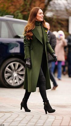 a woman in green coat and black boots walking down the street