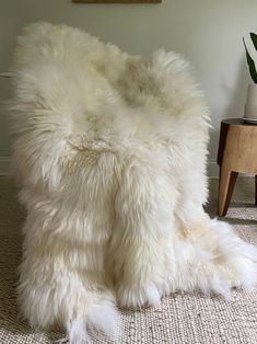 a white furry pillow sitting on top of a rug next to a table with a potted plant