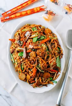 a white bowl filled with noodles and vegetables on top of a table next to utensils