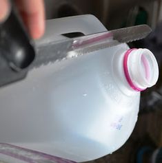 a person holding a bottle with a knife sticking out of it and cutting the top off