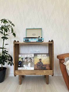 a record player sitting on top of a wooden shelf next to a plant and chair