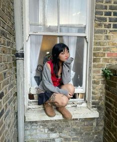 a woman sitting on a window sill in front of a brick building