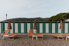 beach chairs and umbrellas are lined up on the sand near an enclosed area with green shutters