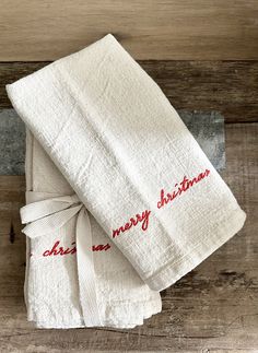 two white towels with red lettering on them sitting on top of a wooden table next to each other