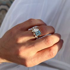 a woman's hand holding a ring with an aqua topazte and diamond center