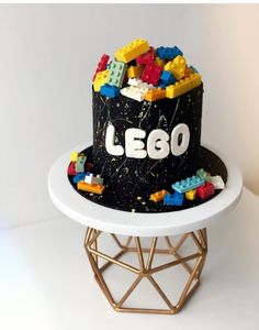 a lego themed birthday cake on top of a white table with gold geometric base and black frosting