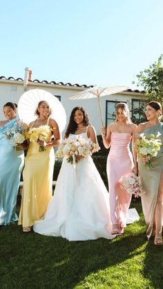 a group of bridesmaids holding umbrellas in front of a house with flowers