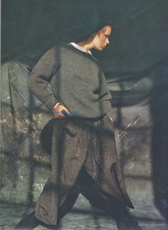 a man is standing with his hands in his pockets while wearing a sweater and pants