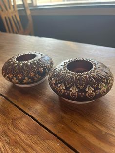 two brown and white vases sitting on top of a wooden table next to a window