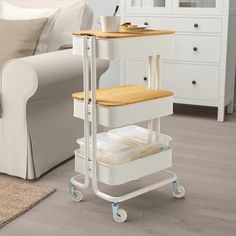 a white cart with two trays on it in front of a couch and coffee table