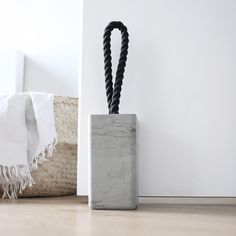 a black rope is sticking out of a concrete container on the floor next to a white wall