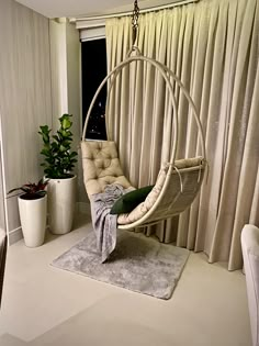 a hanging chair in the corner of a living room with curtains and potted plants