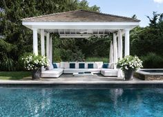 a white couch sitting under a gazebo next to a swimming pool with blue water