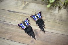 two pairs of beaded butterfly earrings sitting on top of a wooden table next to a potted plant