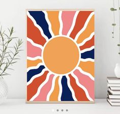 an orange, blue and pink sun print on a white shelf next to some books