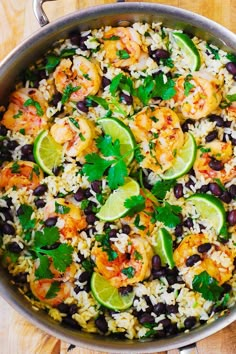 a skillet filled with rice, black beans and limes on top of a wooden table