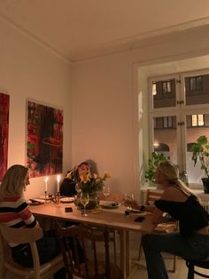 two women sitting at a table with wine glasses and candles in front of the window