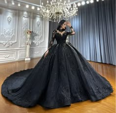 a woman in a black ball gown standing on a wooden floor next to a chandelier