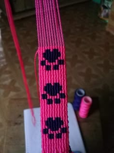 pink and black beaded object on top of a white box next to some spools of thread