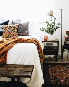 a bed with pillows and blankets on top of it next to a wooden bench in front of a window